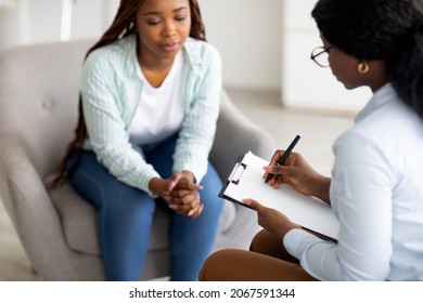 Stressed black female patient consulting psychologist at medical office, selective focus. Psychiatrist helping sad African American woman with nervous problems, taking notes during session - Powered by Shutterstock