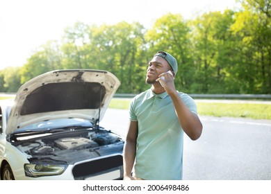 Stressed Black Guy Standing Near Broken Vehice, Having Mobile Phone Conversation With Breakdown Road Service, Asking For Assistance In Car Wreck. African American Man Calling Emergency Help Number