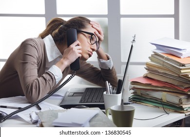A stressed business woman looks tired  she answer telephones in her office