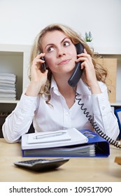 Stressed Business Woman In The Office Using Two Phones Simultaneously