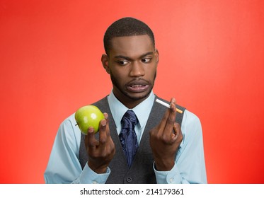 Stressed Businessman Deciding On Healthy Life Choices, Craving Cigarette Versus Green Apple Isolated Red Background. Face Expression, Body Language, Bad, Hazardous Human Habits