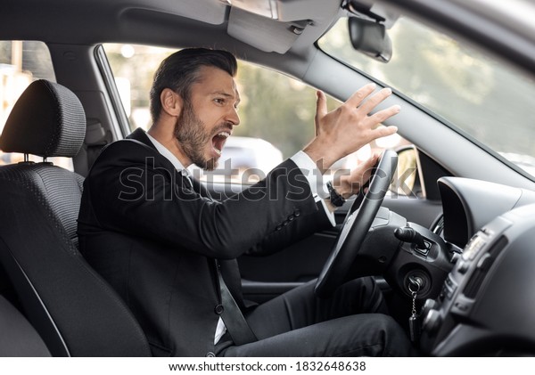 Stressed\
businessman driving luxury car, stuck in traffic, late to airport,\
side view, copy space. Furious middle-aged man in expensive suit\
screaming and gesturing while driving\
auto