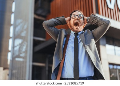 A stressed businessman expressing frustration outdoors in a city environment, captured with an expressive gesture and open mouth, conveying emotions of stress and tension in a business setting. - Powered by Shutterstock