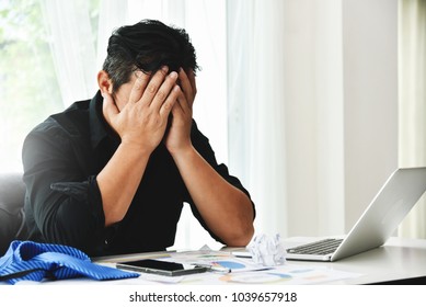 Stressed Businessman Holding Face With His Hands Because Having Trouble. Bankrupt Asian Male Is Sitting With Laptop Computer And Paperwork On Desk At Workplace In Office. Business Mistake Financial.