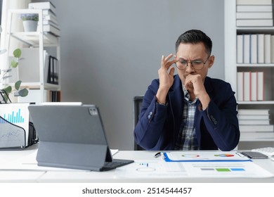 Stressed businessman overwhelmed at office desk analyzing charts, feeling headache from pressure of deadlines and financial reports, exhausted and worried - Powered by Shutterstock