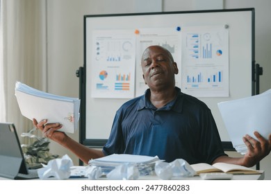 Stressed businessman surrounded by paperwork, charts, and crumpled documents, indicating a busy and chaotic work environment. - Powered by Shutterstock