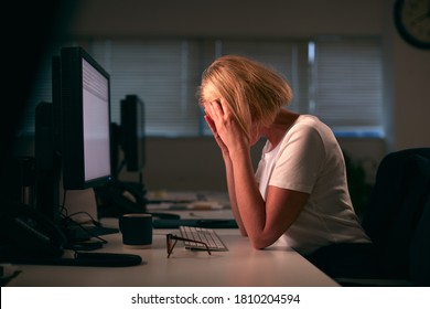 Stressed Businesswoman With Head In Hands Working Late At Computer In Office