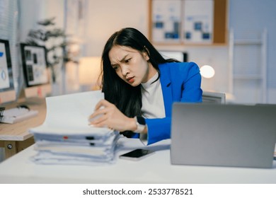 Stressed businesswoman overwhelmed by paperwork at her desk in the office, reflecting career-related stress and mental health toll - Powered by Shutterstock