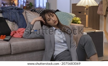 stressed businesswoman seated alone in unorganized living room. woman frowning and letting out soft sigh. seeming to have a lot on her mind.