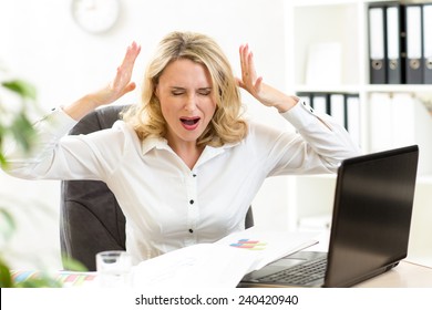 Stressed businesswoman shouting loudly at laptop in office