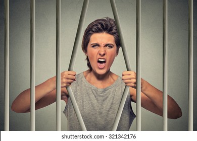 Stressed desperate angry woman bending bars of her prison cell on gray wall background. Life limitations, law violation infringement tax evasion consequences concept. Face expression emotion