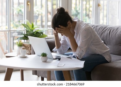 Stressed desperate broke business woman, homeowner getting frustrated at laptop at home, touching head, suffering from headache due to bad news. Financial problems, bankruptcy concept