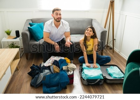 Stressed disorganized man having problems packing his suitcase to travel with her happy beautiful partner 