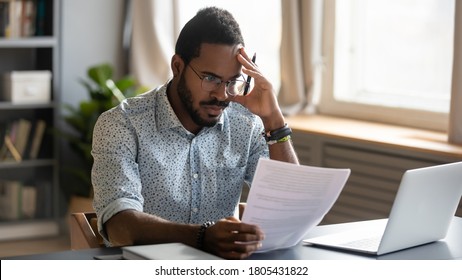 Stressed dissatisfied African American businessman reading letter with bad news, unexpected debt, bank or job dismiss notification, student working on difficult project, holding document in hand