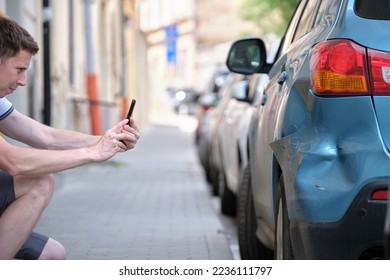Stressed driver taking picture on sellphone camera of smashed vehicle parked on street side calling for emergency service help after car accident. Road safety and insurance concept - Shutterstock ID 2236111797