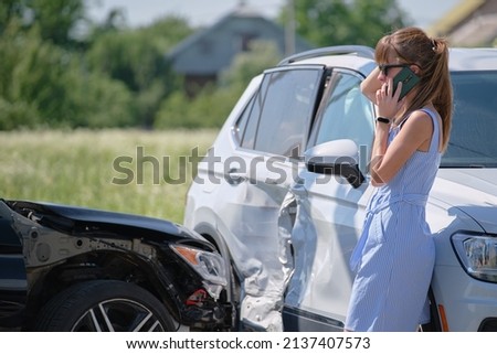 Stressed driver talking on sellphone on roadside near her smashed vehicle calling for emergency service help after car accident. Road safety and insurance concept