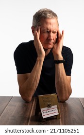 Stressed Elderly Man Eyes Shut Resting On A Dark Wood Table With A White Background