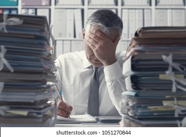 Stressed exhausted business executive in the office overloaded with work, he has stacks of paperwork on the desk