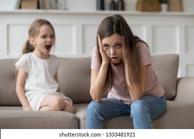 Stressed exhausted mother looking at camera feeling desperate about screaming stubborn kid daughter tantrum, upset annoyed mom tired of naughty difficult child girl misbehave yelling for attention