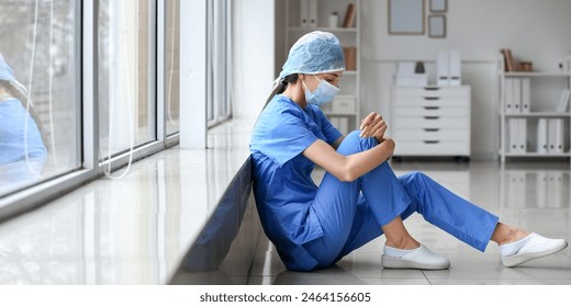 Stressed female surgeon sitting on floor near window in clinic - Powered by Shutterstock