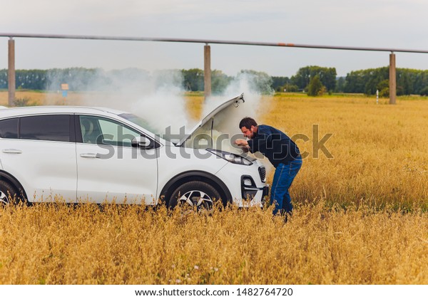 Stressed and frustrated driver pulling his hair\
while standing on the road next to broken car. Road trip problems\
and assistance concepts.\
smoke.