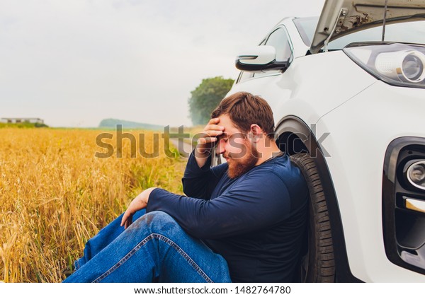 Stressed and frustrated driver pulling his hair\
while standing on the road next to broken car. Road trip problems\
and assistance concepts.\
smoke.