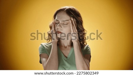 Stressed frustrated young woman feeling pain unwell dizzy, tired of difficult job, suffering from panic attack, hormone imbalance or having headache migraine massaging temples. Yellow background [[stock_photo]] © 
