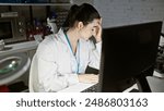 A stressed hispanic woman in a lab coat exhibits exhaustion while working in a laboratory.