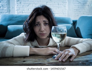 Stressed And Hopeless Young Woman Drinking A Glass Of Wine Alone At Home. Feeling Depressed, Frustrated And Weak, Trying To Feel Better Drinking. Unhealthy Behavior, Depression And Alcoholism Concept.