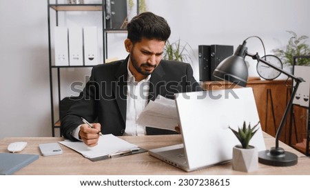 Stressed indian businessman working looking at unpaid bank debt bills, doing paperwork, planning budget, calculate finances mortgage payments at office. Displeased freelancer man throws paper bills