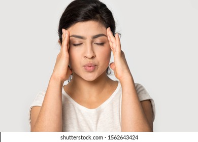 Stressed Indian girl massaging temples close up isolated on grey studio background, unhappy young woman with closed eyes suffering from headache, feeling pain, tension, migraine, health problem - Powered by Shutterstock