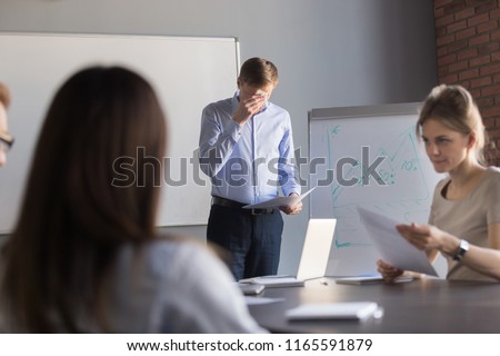 Stressed male speaker or presenter worried before making presentation for colleagues in meeting room, nervous employee wipe face scared to speak in public, afraid to present business report in office.