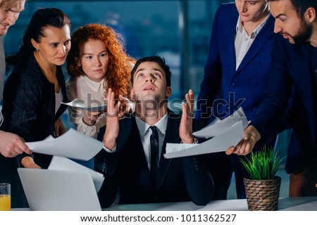 stressed male worker raises his hands and says please God while his colleagues ask him to do the job