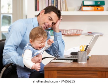 Stressed Man With Baby Working From Home Using Laptop