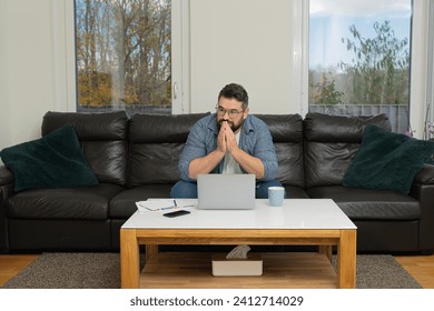 A stressed man deep worried thinking while working on a laptop at home. - Powered by Shutterstock