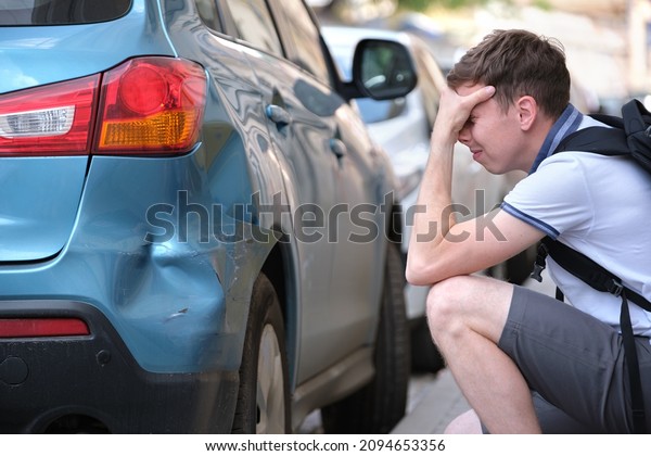 Stressed man driver sitting\
on street side shocked after car accident. Road safety and\
insurance concept