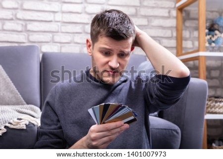 Stressed Man Looking At Too Many Credit Cards In Home