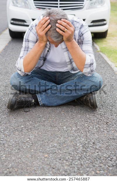Stressed man\
sitting on the ground beside his\
car
