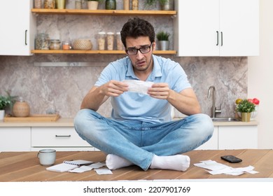 Stressed man sitting on the table and holding many bills in his hands in a spending, taxes and debt concept	 - Shutterstock ID 2207901769