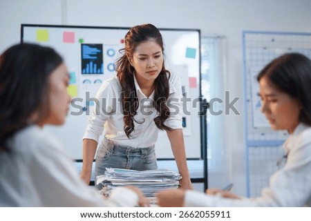 Stressed manager looking down at her colleagues during an office meeting, with graphs and charts on the whiteboard behind her