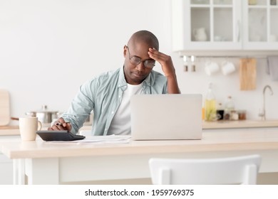 Stressed Mature Black Man Using Calculator And Laptop Computer, Calculating Taxes, Checking Monthly Expenses And Bills, Sitting In Kitchen Interior At Home, Copy Space