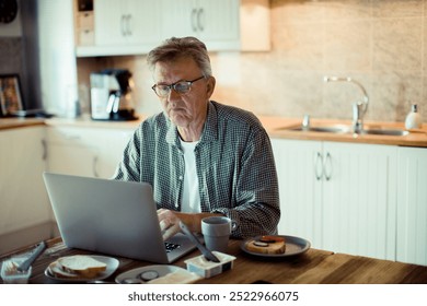 Stressed mature man using laptop on kitchen table during breakfast - Powered by Shutterstock