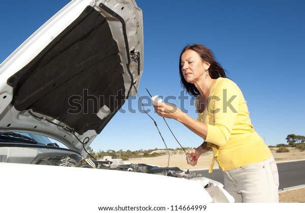 Stressed mature woman\
breakdown with car on remote road checking oil and waiting for\
assistance, for help, isolated with blue sky as background and copy\
space.