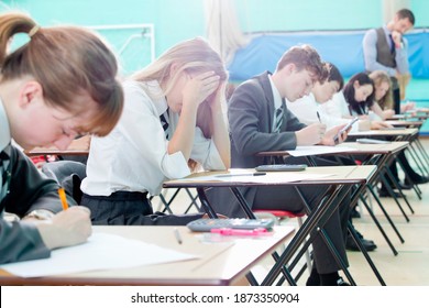 Stressed Middle School Student Taking Examination At Desks In School Gymnastics Hall