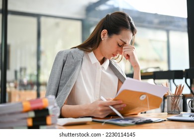Stressed millennial Asian businesswoman feeling upset and depressed after reading a document, receiving a termination letter while working at her desk.
