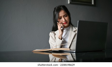 Stressed Millennial Asian Businesswoman Or Female Manager Having A Serious Phone Call With Her Business Client While Working In The Office.