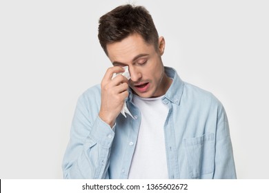 Stressed millennial Caucasian man isolated on grey studio background feel bad or down, depressed European male in blue shirt suffer from depression cry wipe tears using napkin or tissue