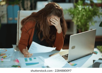 stressed modern middle aged small business owner woman working with documents in the modern green office.