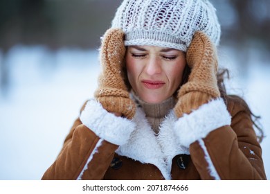 Stressed Modern Woman With Mittens In A Knitted Hat And Sheepskin Coat Outside In The City Park In Winter.