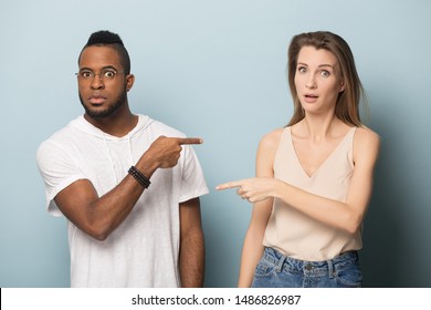 Stressed multicultural young man and woman isolated on blue studio background point finger at each other, surprised frustrated african American male and Caucasian female blame accuse one another